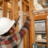 A construction worker connecting plumbing pipe in an unfinished wall. Focus is on the connecting pipes.